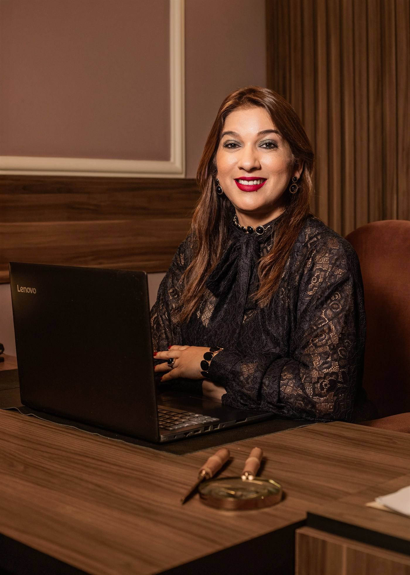 Juliana Araújo sorrindo, sentada à mesa do escritório com o notebook aberto